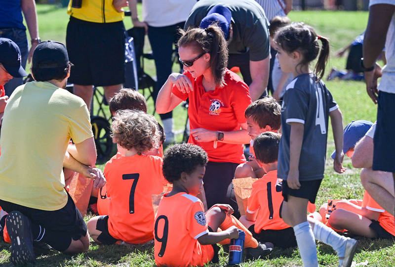 A Region 13 coach giving instruction to a team of young players gathered around