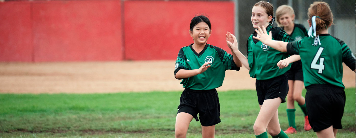 Region 13 girls in green and black uniforms celebrate together on the field
