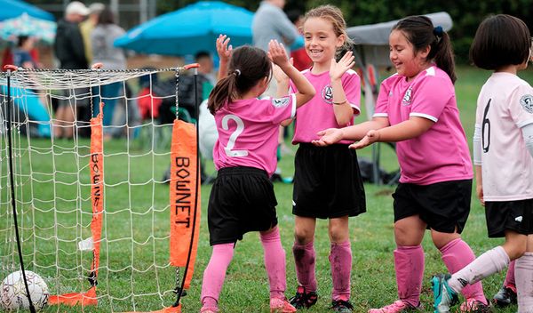 Young Region 13 players in pink uniforms high-five after a play