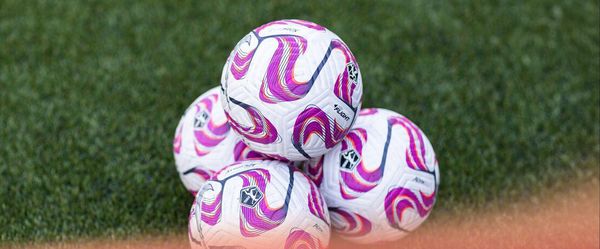 A stack of pink and white Angel City FC soccer balls on grass