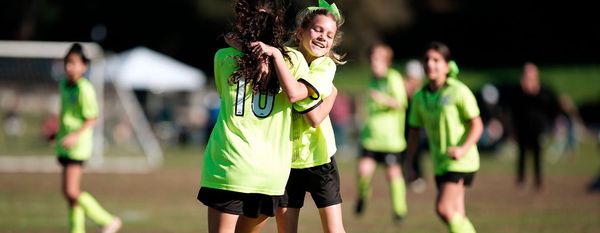 Two Region 13 teammates in lime green uniforms hug after a play